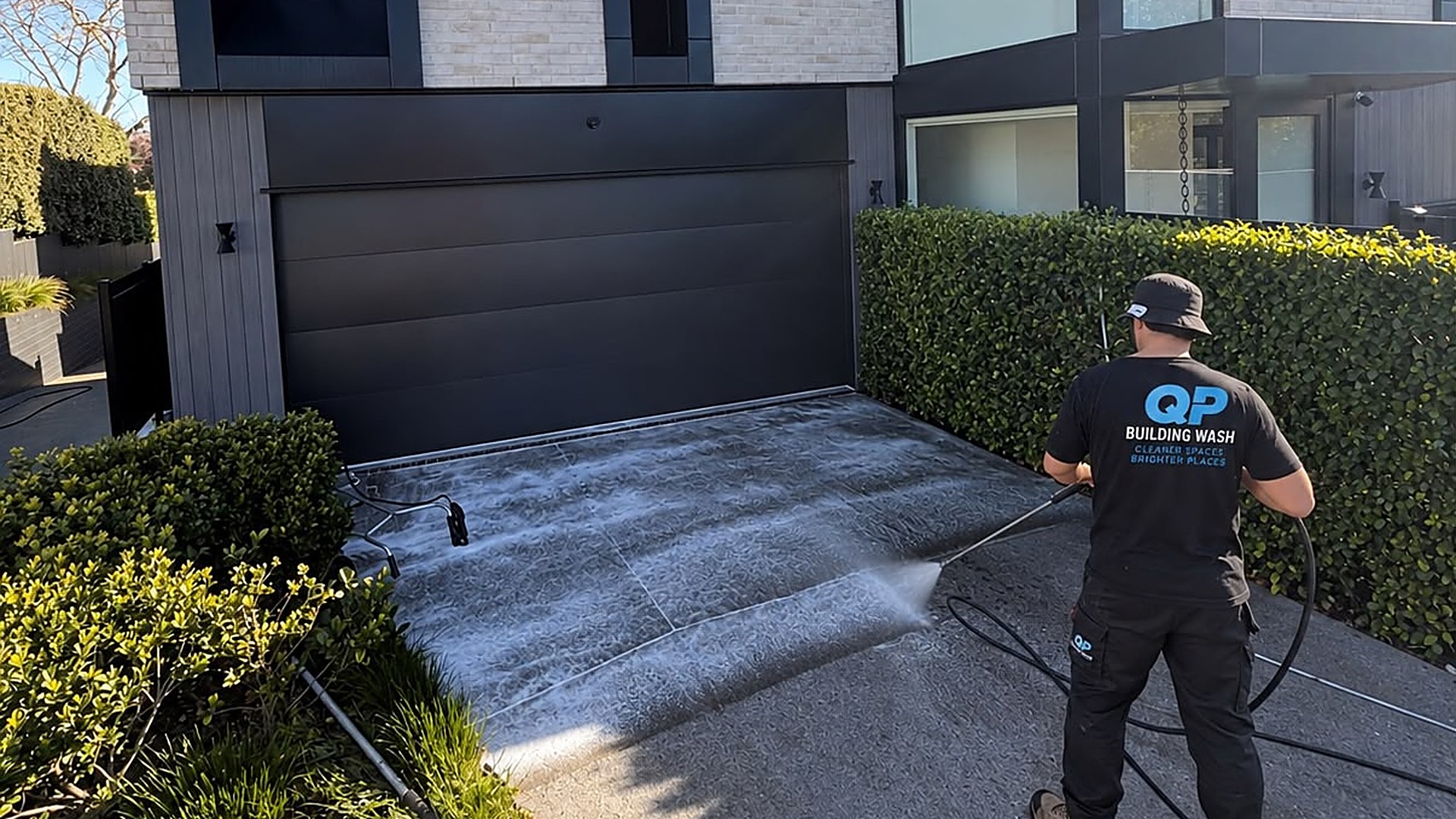 QP Building Wash team member water blasting a concrete driveway