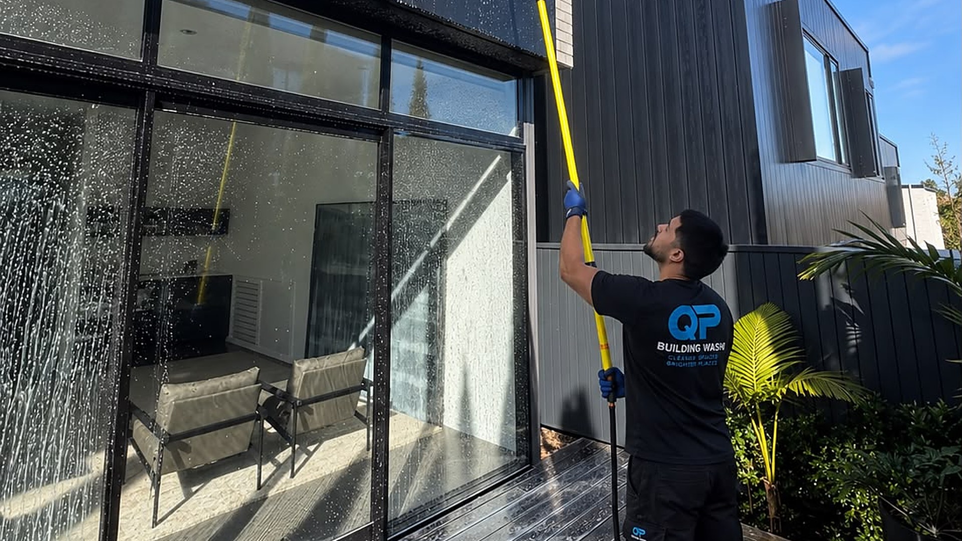QP Building Wash team member washing upper storey windows with a pole and brush